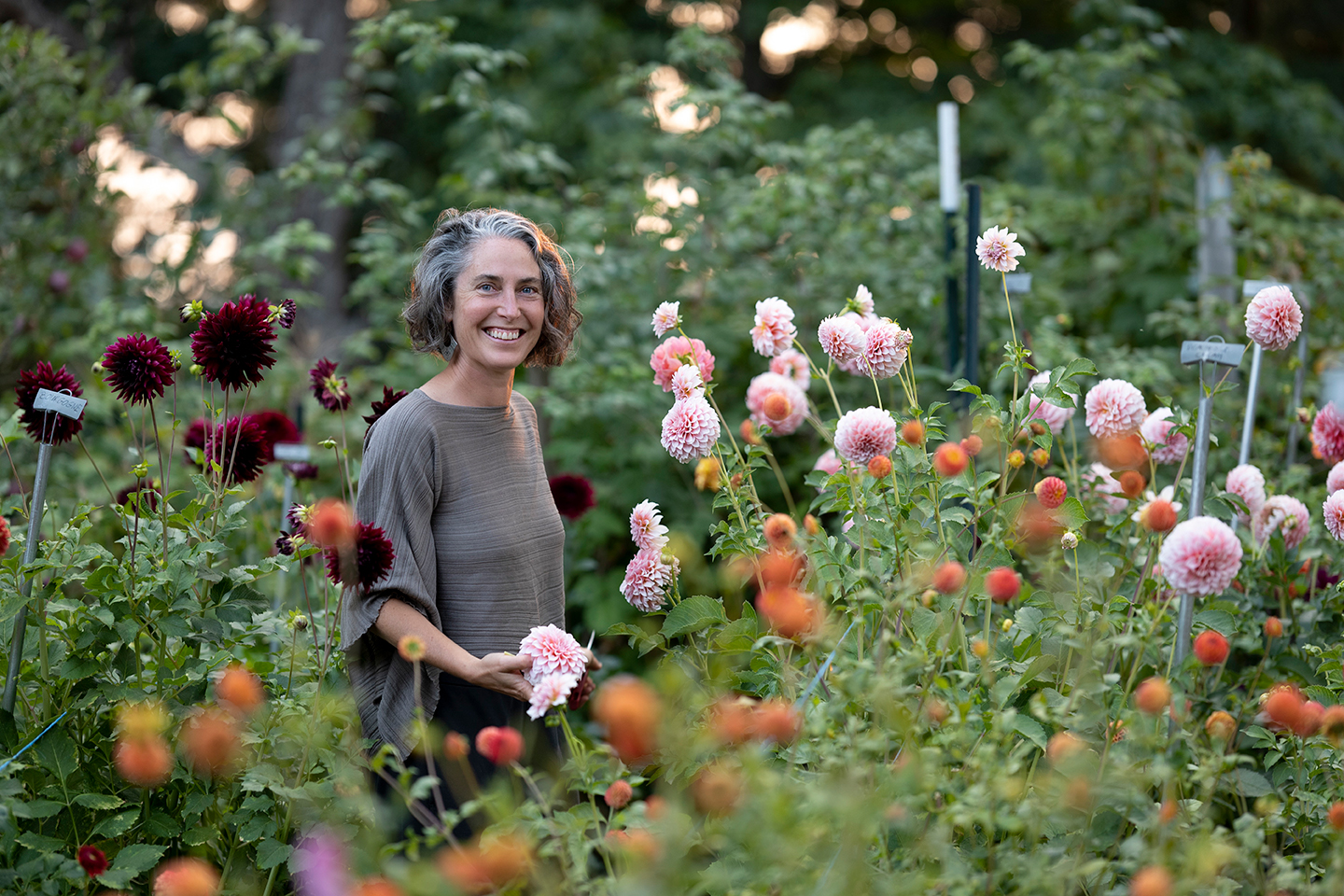 Portrait of Julie Rémy, owner of Fleuris Orchard & Blooms surrounded by dahlias growing in front of a forested area of the farm.